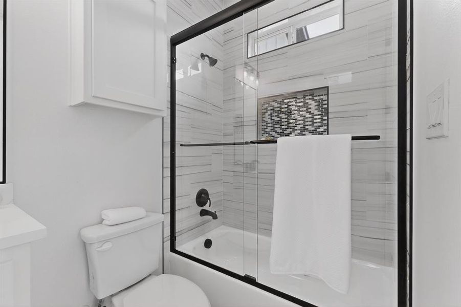 Bathtub with matte black fixtures and a glass shower enclosure featuring white horizontal subway tile