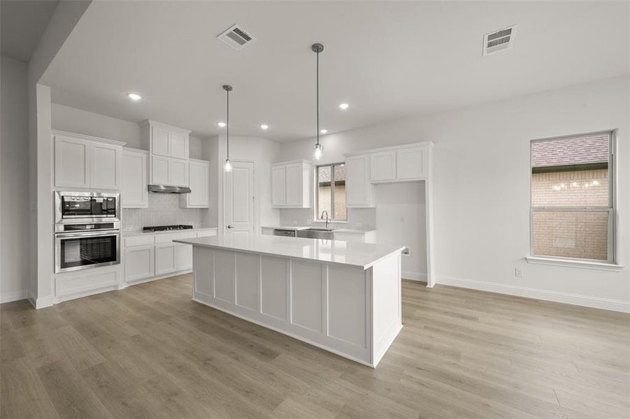Kitchen with appliances with stainless steel finishes, white cabinets, light countertops, light wood-style floors, and decorative backsplash Kitchen with appliances with stainless steel finishes, white cabinets, light countertops, light wood-style floors, and decorative backsplash
