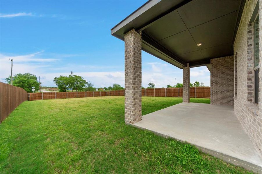 Expansive backyard featuring a covered patio with brick columns, a concrete slab, and a recessed light fixture