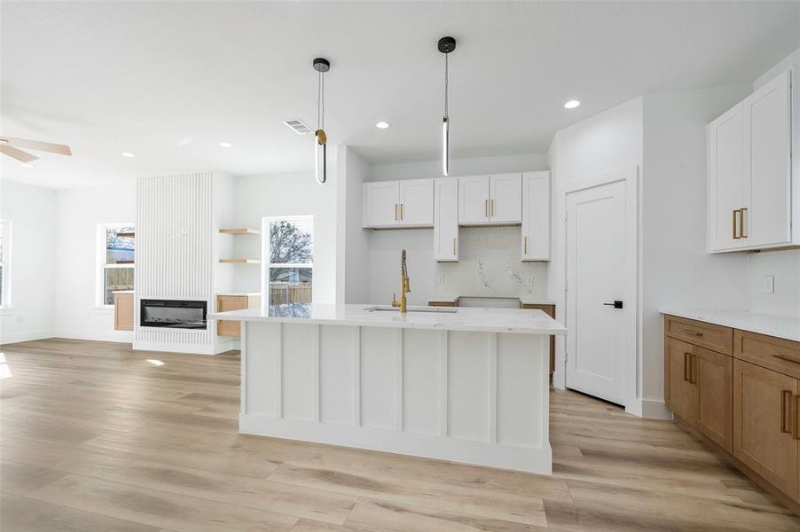 Kitchen with white cabinets, light hardwood / wood-style floors, a kitchen island with sink, and hanging light fixtures