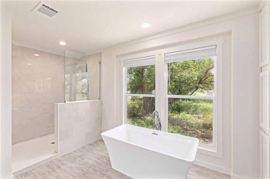 Freestanding soaking tub with chrome fixtures, accompanied by a walk-in shower featuring a glass enclosure and tiled walls