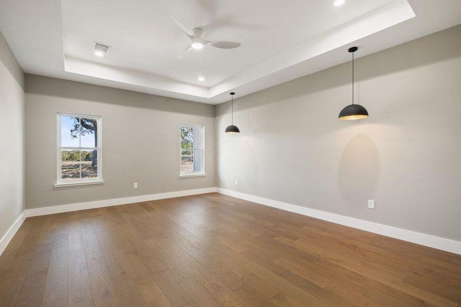 Empty room featuring a raised ceiling, hardwood / wood-style flooring, a ceiling fan, and recessed lighting