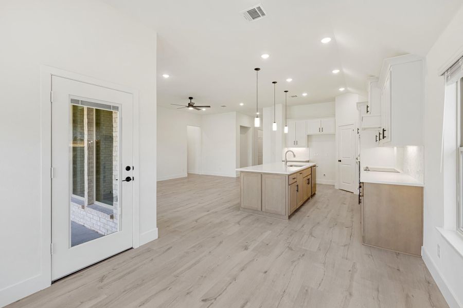 Open kitchen with white cabinets, center island, pendant lights, and light wood floors leading to living area