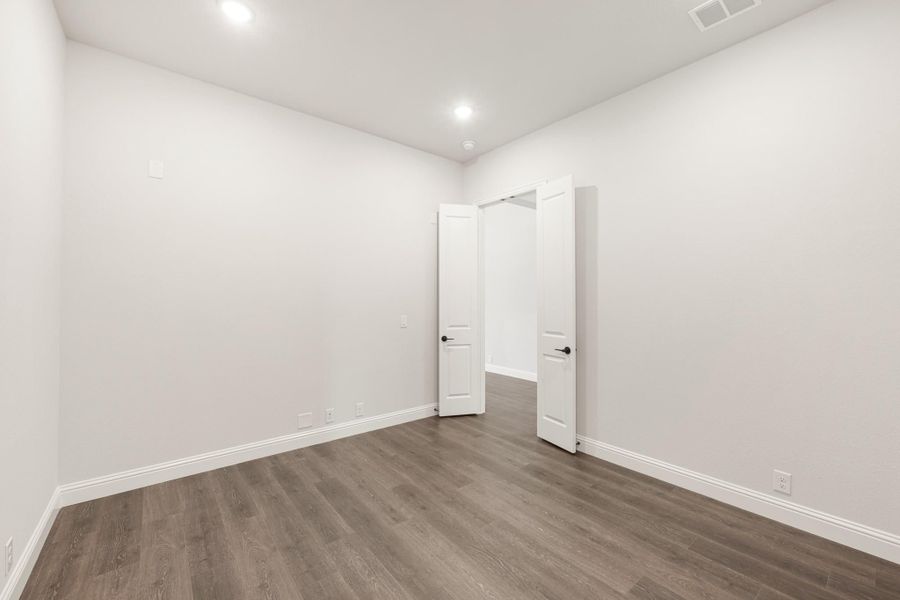 Empty bedroom with white walls, dark hardwood floors, and two white panel doors Empty bedroom with white walls, dark hardwood floors, and two white panel doors