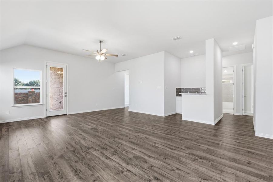 Spacious living area featuring wood-finish flooring, vaulted ceilings, and a ceiling fan with integrated lighting