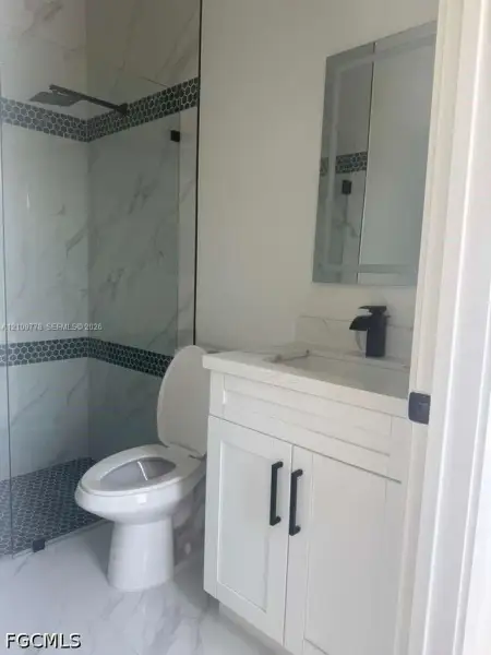 Bathroom featuring a glass-enclosed shower with tiled walls and decorative border, vanity with stone-composite countertop, matte black faucet, and frameless illuminated mirror Bathroom featuring a glass-enclosed shower with tiled walls and decorative border, vanity with stone-composite countertop, matte black faucet, and frameless illuminated mirror