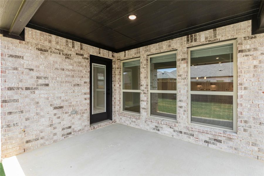 Covered back patio with brick walls, dark ceiling, recessed light, and large windows overlooking the backyard