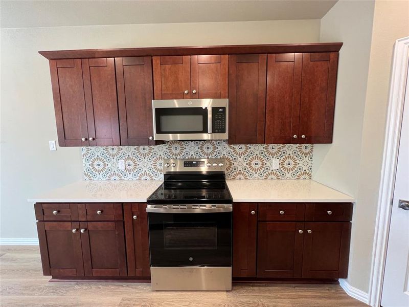 Kitchen with appliances with stainless steel finishes, light hardwood / wood-style floors, and tasteful backsplash