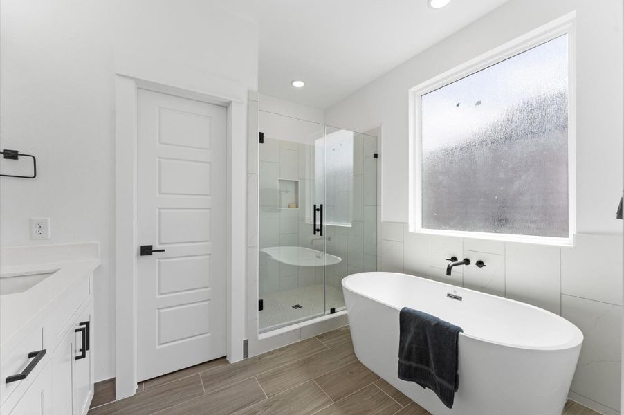 Indulge in everyday luxury in this elegant primary bathroom, where a freestanding soaking tub and a spacious walk-in shower offer the best of both worlds. The frameless glass shower enclosure showcases elegant tilework and dual showerheads, while the tub invites relaxation beneath a statement light fixture. A double vanity with quartz countertops and individual mirrors adds modern sophistication, and soft neutral tones create a serene, spa-like ambiance that elevates your daily routine.