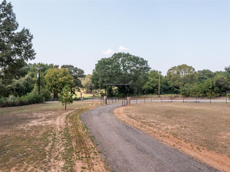 View of dirt / gravel driveway featuring a view of rural / pastoral area and a gated entry