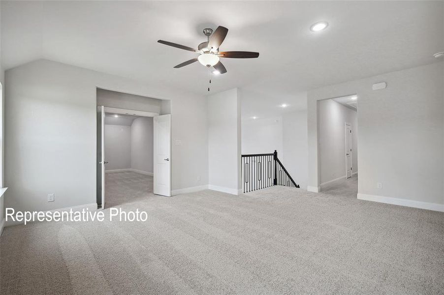 Expansive carpeted room featuring a ceiling fan with integrated lighting, recessed lighting, and a black wrought iron staircase railing