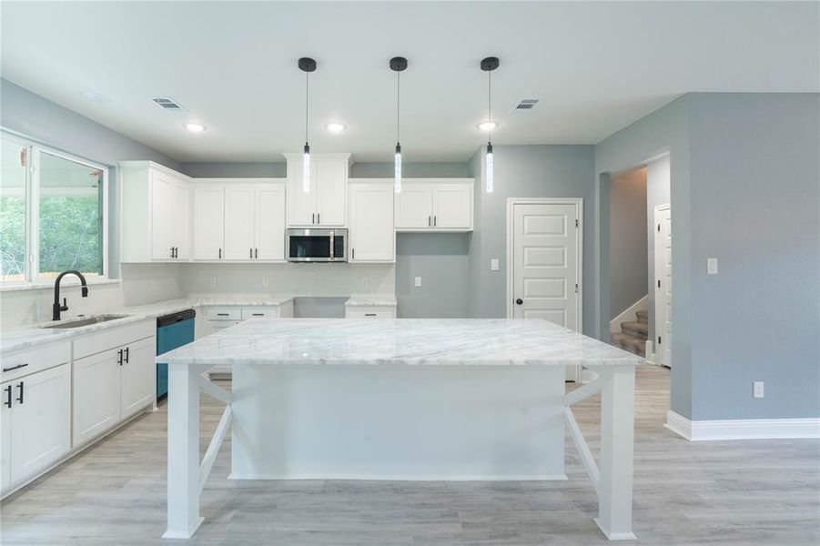 Kitchen with dishwasher, light stone countertops, light hardwood / wood-style flooring, sink, and a kitchen island