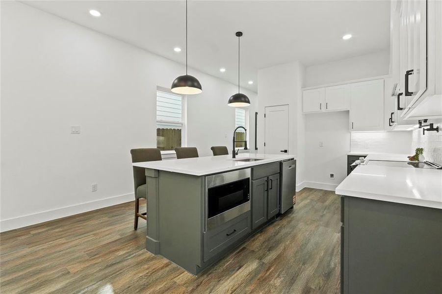 Kitchen featuring a kitchen bar, two tone cabinets, an island with sink, stainless steel appliances, and dark wood-type flooring Kitchen featuring a kitchen bar, two tone cabinets, an island with sink, stainless steel appliances, and dark wood-type flooring
