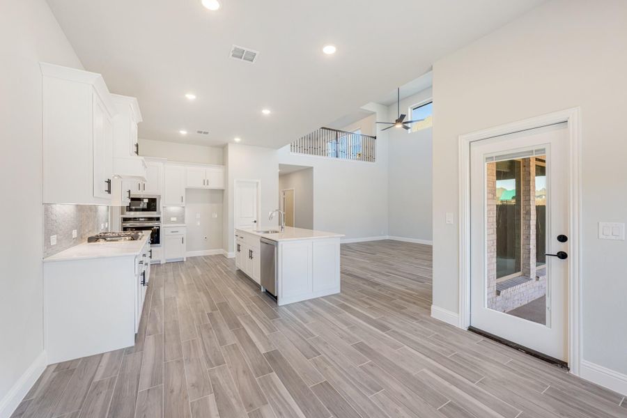 Open-concept kitchen with white cabinets, center island, stainless appliances, and wood-look tile floors Open-concept kitchen with white cabinets, center island, stainless appliances, and wood-look tile floors