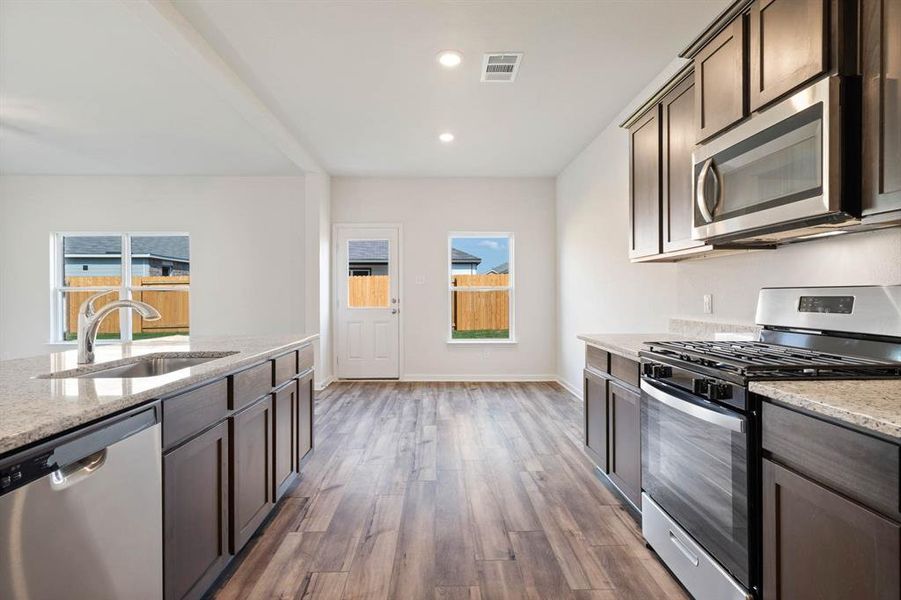 Kitchen featuring appliances with stainless steel finishes, sink, light stone counters, and dark hardwood / wood-style flooring