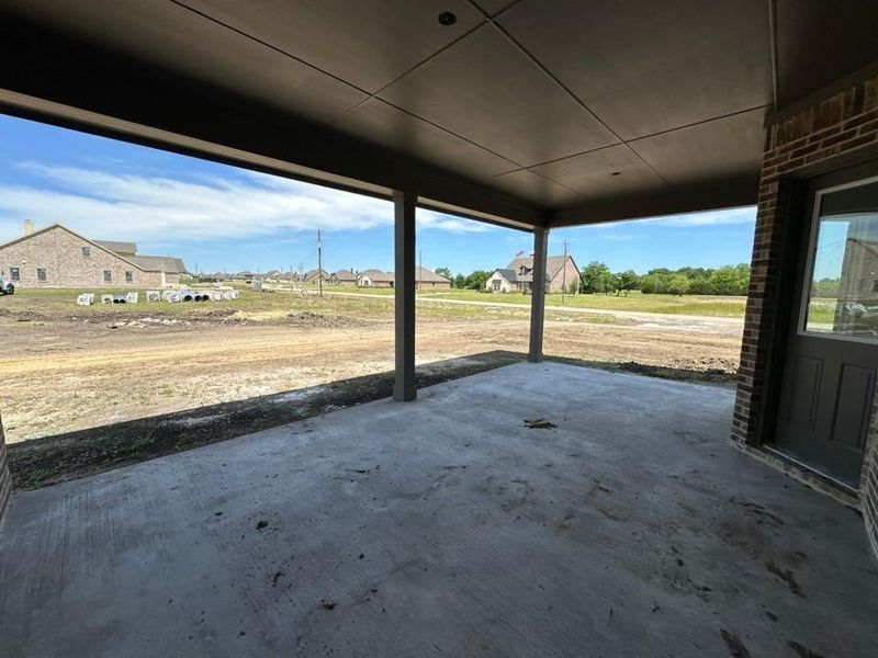 Covered concrete patio with recessed lighting, supported by two columns, featuring a brick exterior wall and a panel door