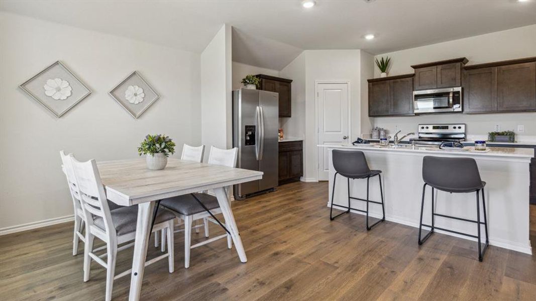 Kitchen featuring stainless steel appliances, dark wood finish cabinets, a breakfast bar area, dark wood-style flooring, and a kitchen island with sink