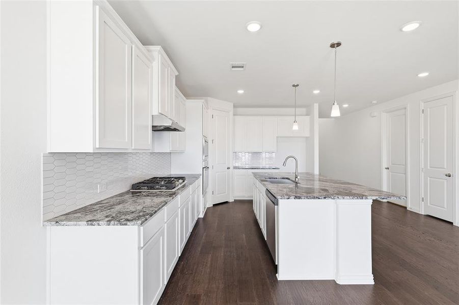 Open-concept kitchen featuring an expansive central island with an undermount sink, pendant lighting, stainless steel appliances, white shaker cabinetry, and wood-finish flooring