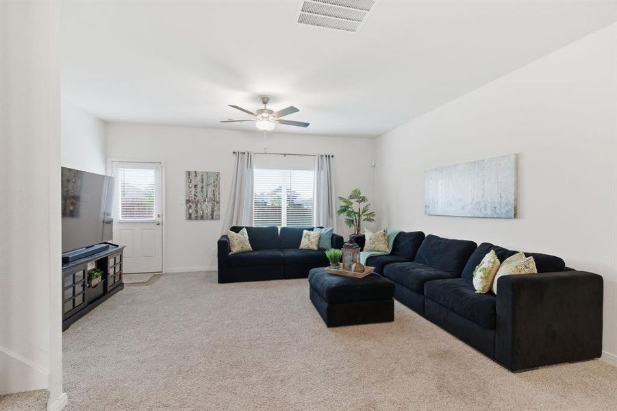 Spacious living area featuring light-colored carpeting, a ceiling fan, and ample natural light from the windows