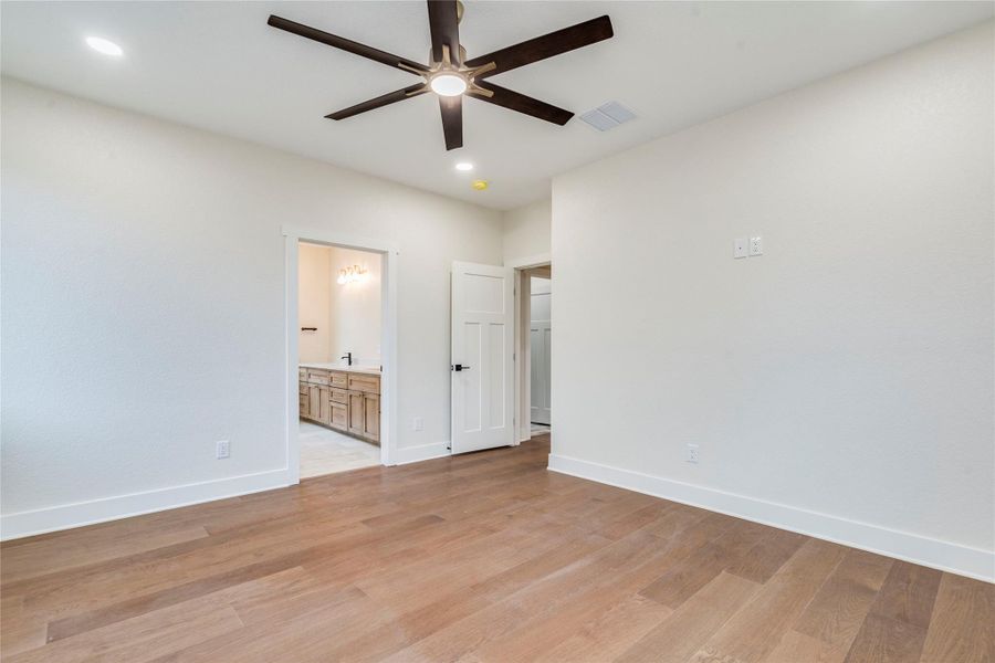 Unfurnished bedroom with connected bathroom, light wood-style flooring, a ceiling fan, and recessed lighting
