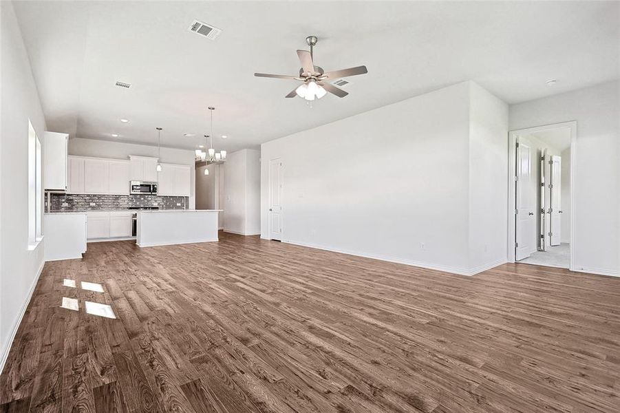 Unfurnished living room with ceiling fan with notable chandelier and hardwood / wood-style flooring