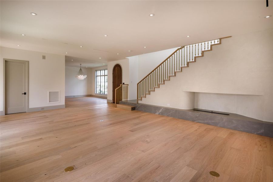 Fresh white oak floors run beneath an open, airy living space where the long plaster fireplace and brass-detailed staircase turn two functional necessities into the room's defining design features.
