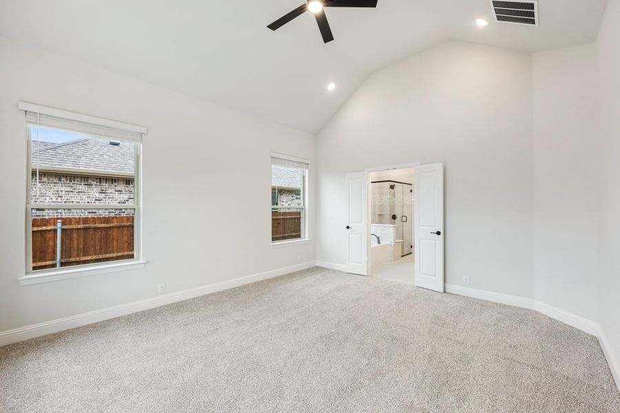Spacious master bedroom with vaulted ceiling, ceiling fan, carpet floors, and open ensuite bathroom door