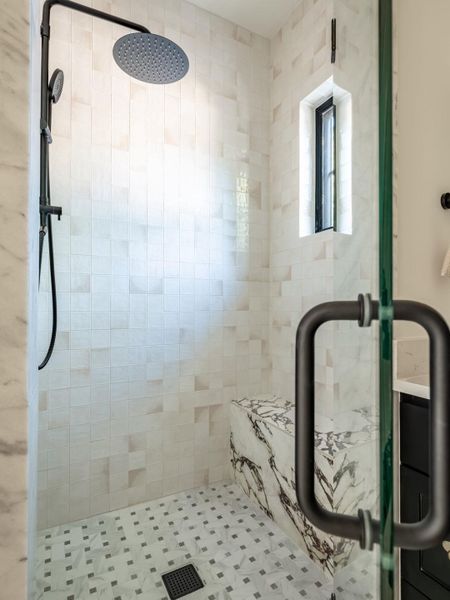 Marble accents and a modern rainfall showerhead define this pristine, well-appointed bathroom.