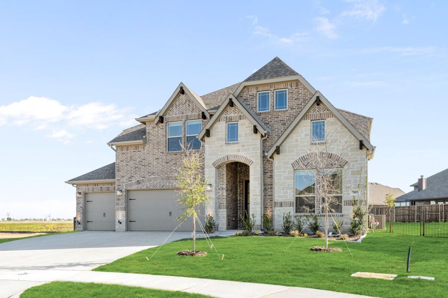 Two-story brick and stone home with three-car garage, arched entry, and manicured front lawn