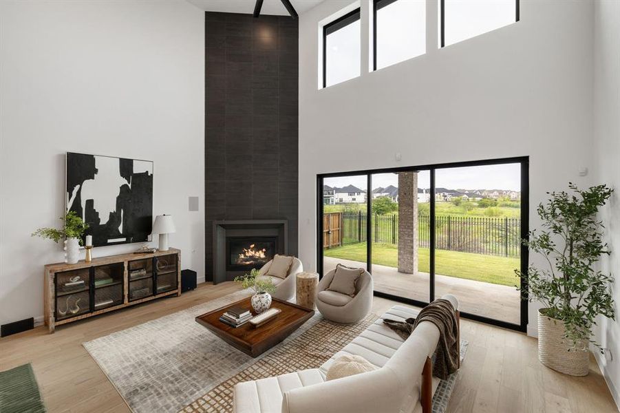 Living room featuring a large fireplace, light wood finished floors, and a high ceiling Living room featuring a large fireplace, light wood finished floors, and a high ceiling