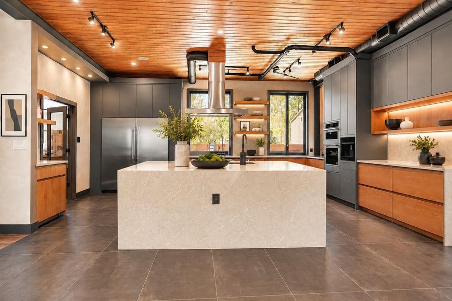 The open-concept design flows into a dining area, highlighted by a wooden ceiling and ample lighting. Large windows bring in natural light, enhancing the inviting atmosphere.