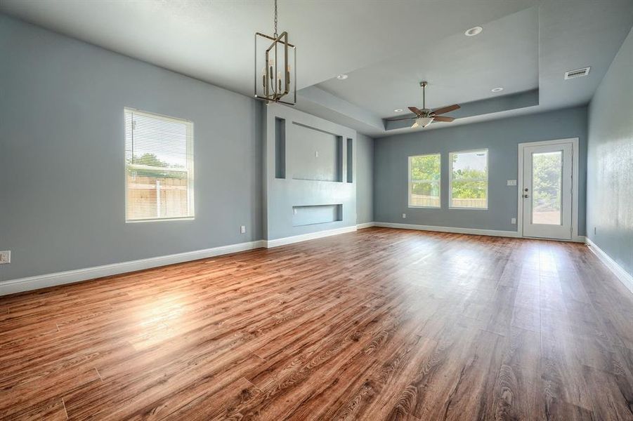 Unfurnished living room featuring ceiling fan with notable chandelier, wood-type flooring, and a tray ceiling