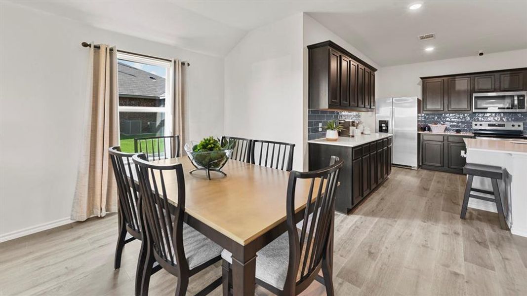 Well-appointed dining area and kitchen featuring light-toned flooring, dark cabinetry, and stainless steel appliances