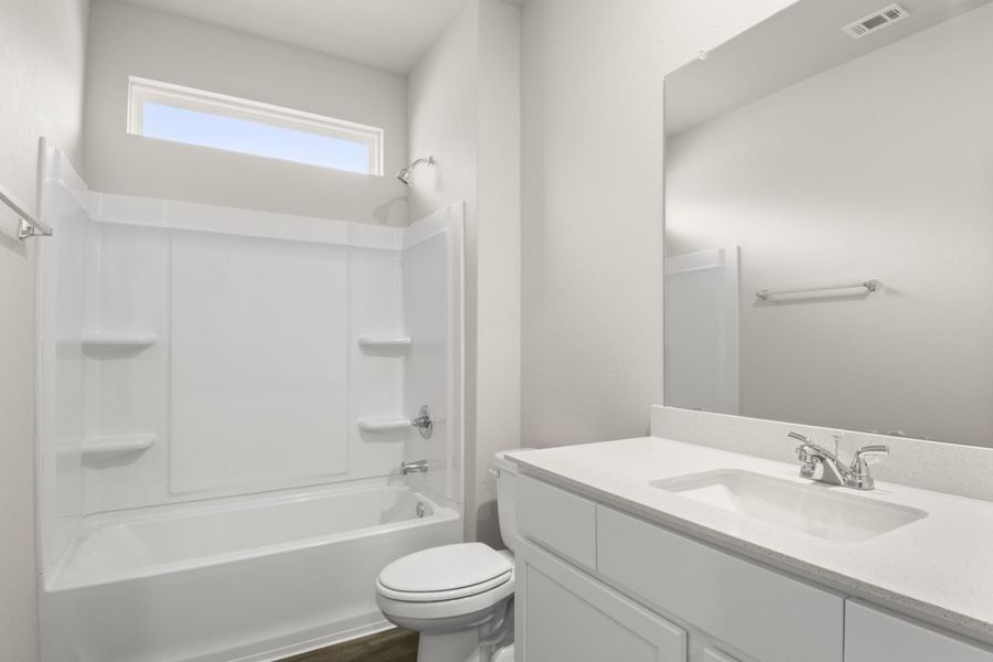 Image of bathroom with white cabinets and vanity with a mirror and a window above the shower and tub