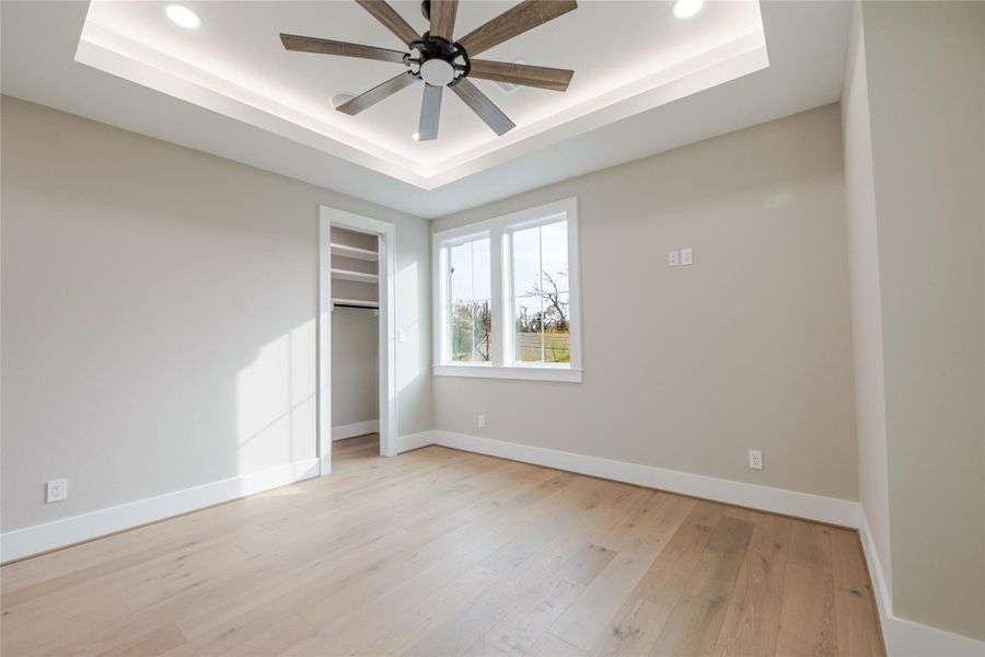 Unfurnished bedroom with a ceiling fan, light wood finished floors, a raised ceiling, and recessed lighting