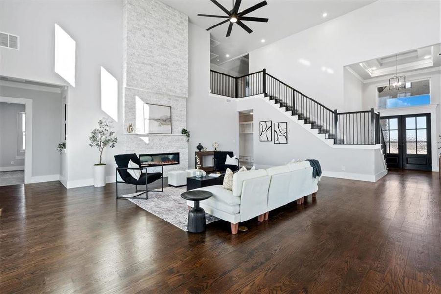 Living room with a towering ceiling, dark hardwood / wood-style floors, a notable chandelier, a stone fireplace, and french doors