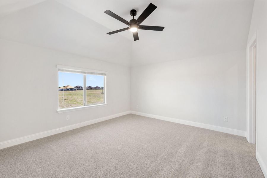 Empty bedroom with vaulted ceiling, black ceiling fan, carpet flooring, and a single window with outdoor views Empty bedroom with vaulted ceiling, black ceiling fan, carpet flooring, and a single window with outdoor views