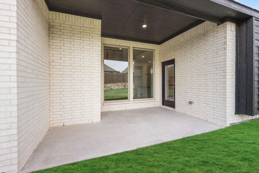 Covered back patio with concrete floor, white brick walls, sliding glass door, and green lawn