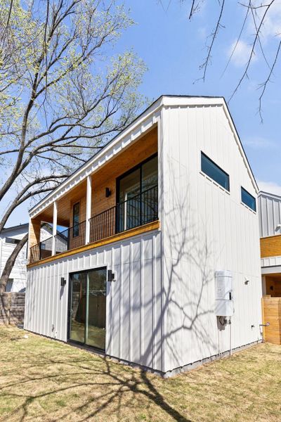 Back of property with a balcony, a yard, and board and batten siding