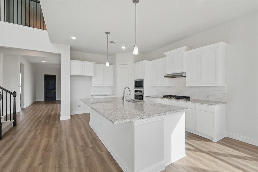 Kitchen featuring light wood-style flooring, appliances with stainless steel finishes, under cabinet range hood, and tasteful backsplash Kitchen featuring light wood-style flooring, appliances with stainless steel finishes, under cabinet range hood, and tasteful backsplash