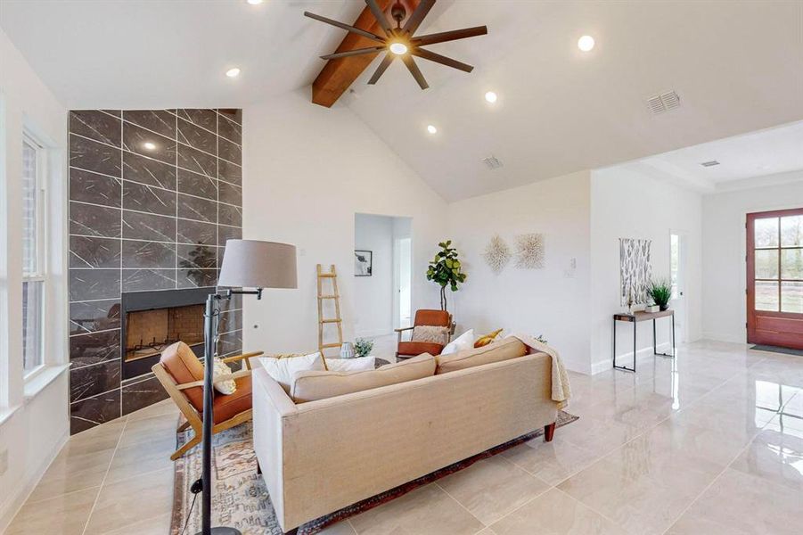 Living room featuring tile walls, vaulted ceiling with beams, a tile fireplace, and ceiling fan