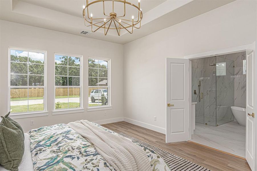Spacious bedroom featuring wood-finish flooring and a contemporary chandelier