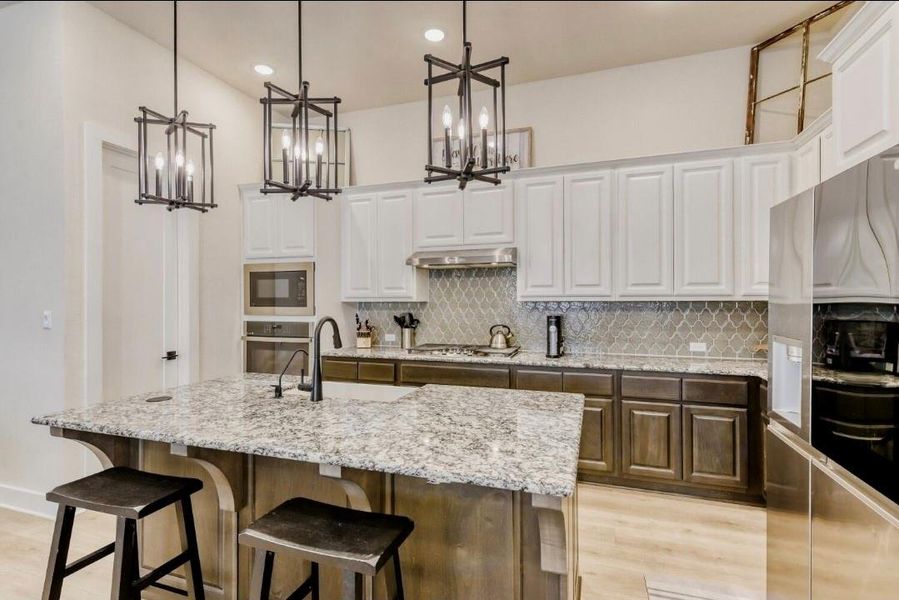 Dual tone kitchen featuring stainless steel appliances, a kitchen breakfast bar, light stone counters, light wood-type flooring, and a kitchen island with sink