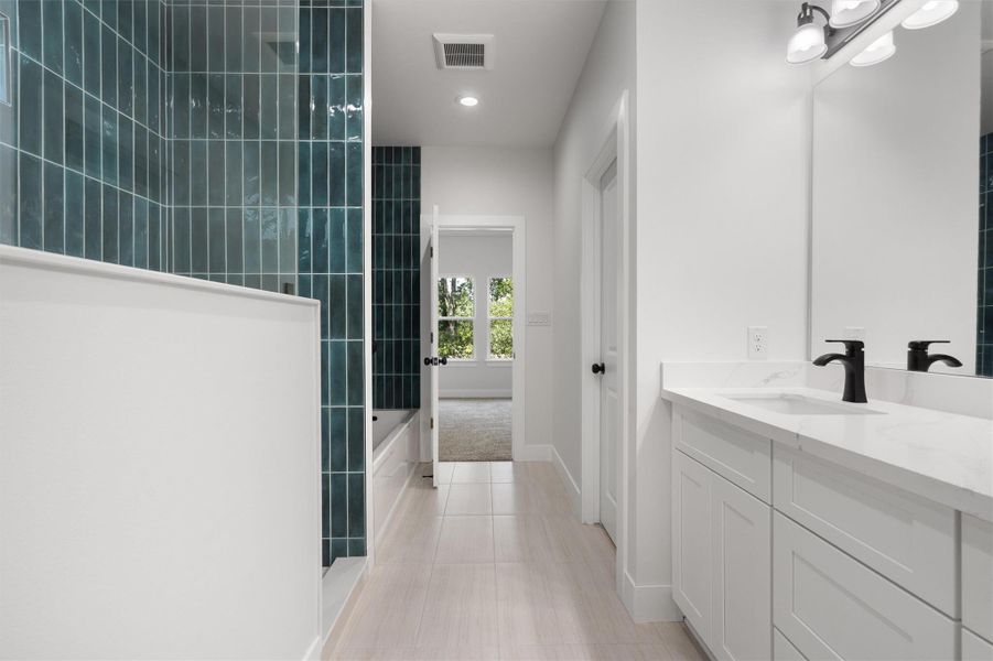 Bathroom featuring a dual vanity with white cabinetry, matte black fixtures, and a spacious tub with teal vertical tile surround