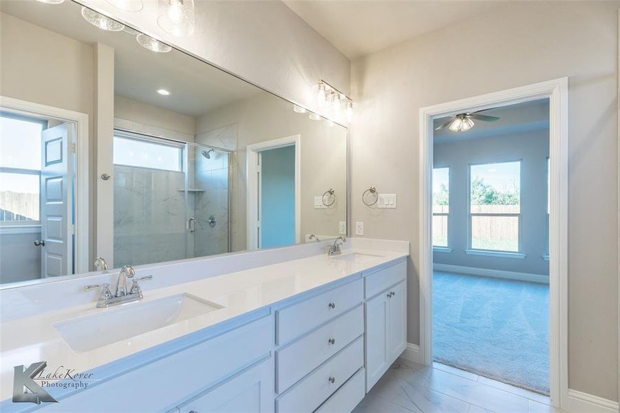 Full bathroom featuring double vanity, a marble finish shower, and light carpet