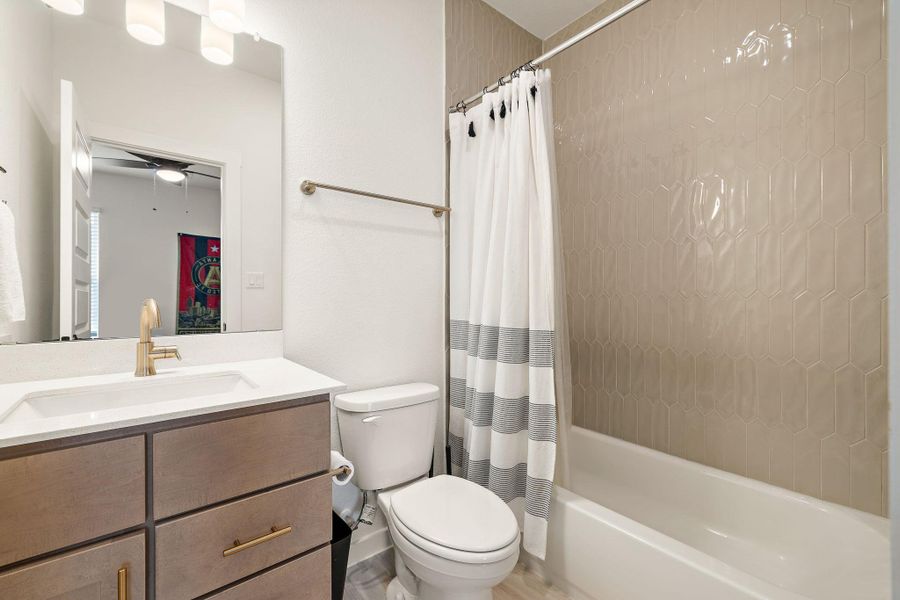 Contemporary bathroom featuring a modern vanity with a white countertop and rectangular undermount sink, brushed gold faucet, and a shower/tub combination with light-toned hex-patterned wall tile