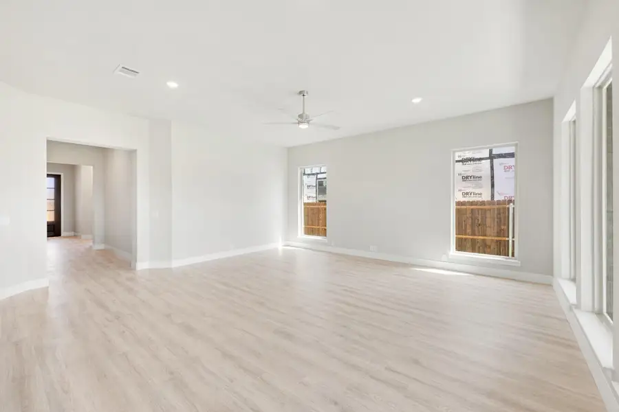 Empty living room with light wood floors, ceiling fan, and two windows with white walls