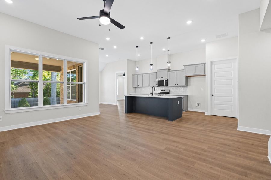 Open-concept layout featuring wood-finish flooring, a kitchen island with seating, pendant lighting, and a multi-pane window Open-concept layout featuring wood-finish flooring, a kitchen island with seating, pendant lighting, and a multi-pane window