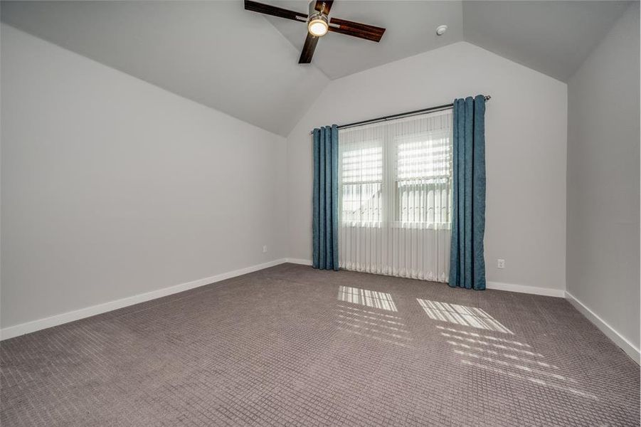 Empty room featuring vaulted ceiling, carpet, baseboards, and ceiling fan