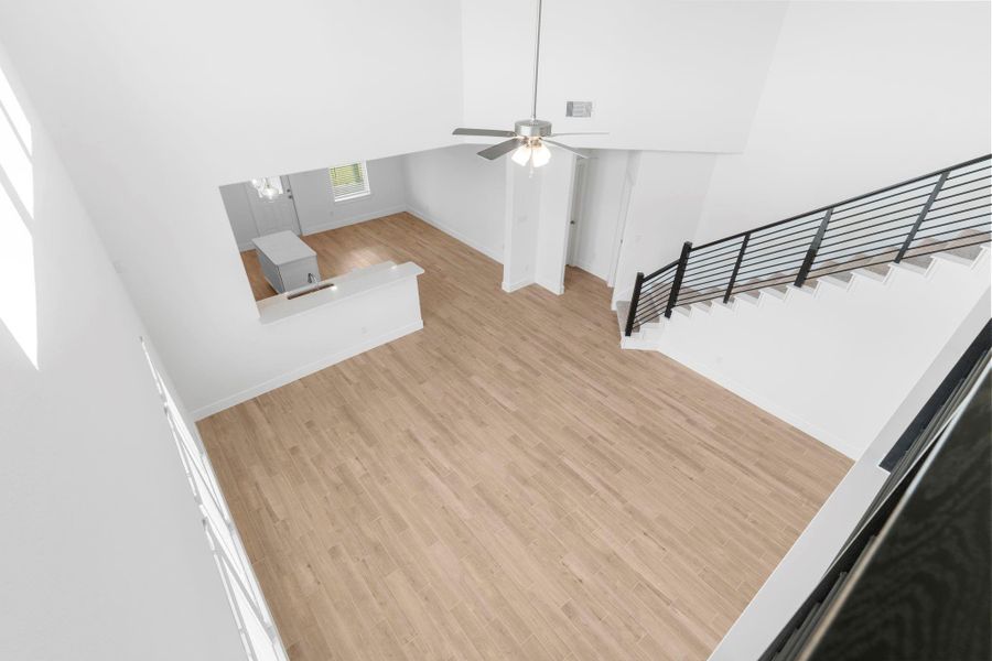 Striking bird’s-eye view from upstairs into the two-story family room, highlighting soaring ceilings, dramatic windows, and the elegant modern iron staircase — call now to see it in person! **Image Representative of Plan Only and May Vary as Built**.